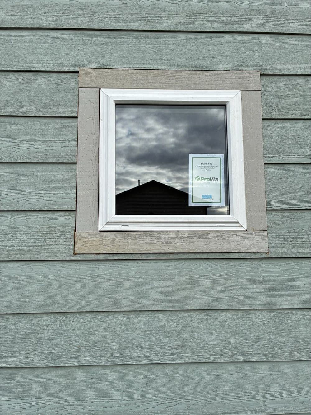 Window reflecting clouds and a house, featuring a notice on the glass.