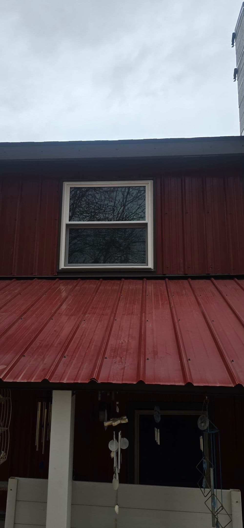 Red metal roof with a window on a wooden building against a grey sky.