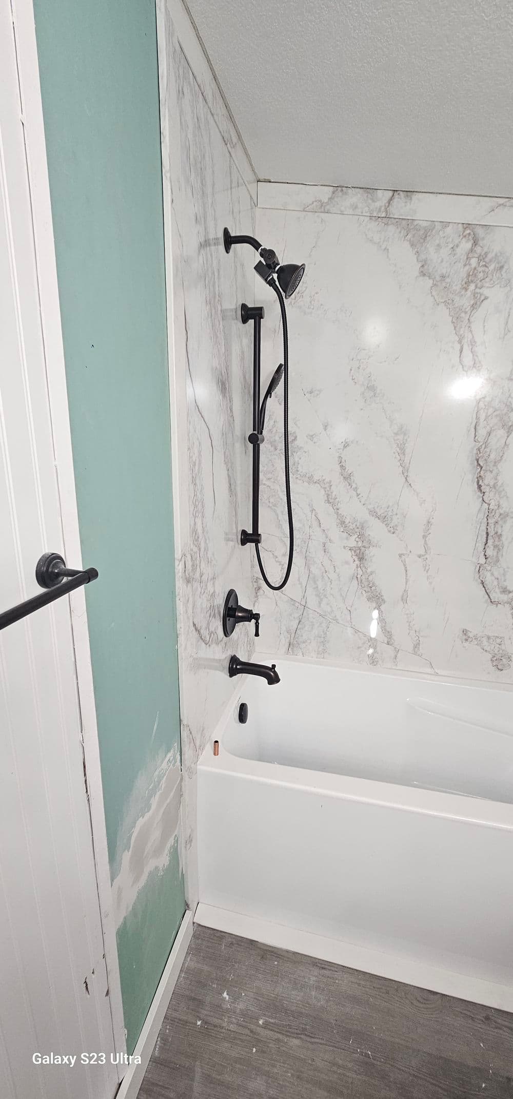 Modern bathroom featuring a marble wall, tub, and black shower fixture. Renovation in progress.
