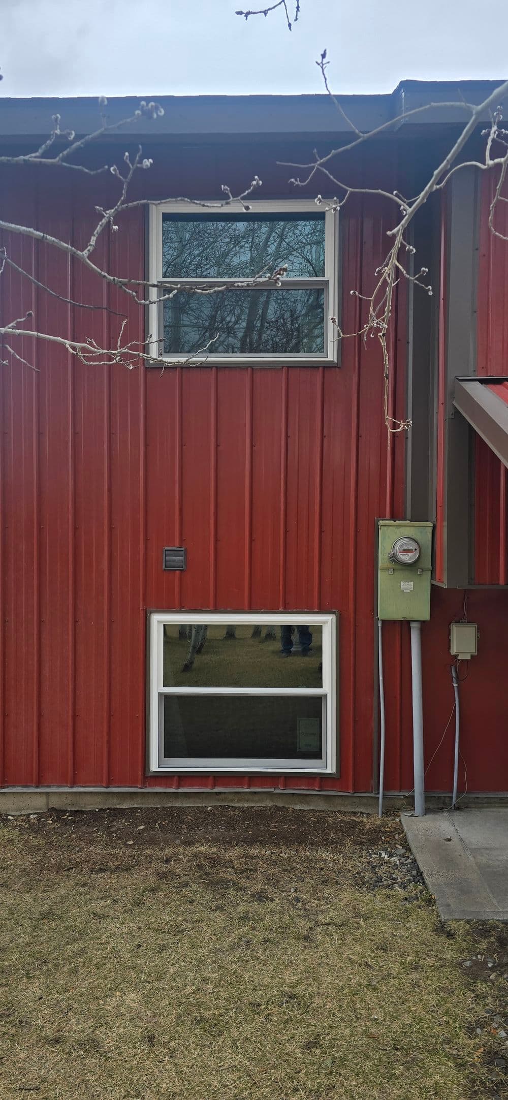 Red metal-clad house exterior featuring two windows and an electric meter.