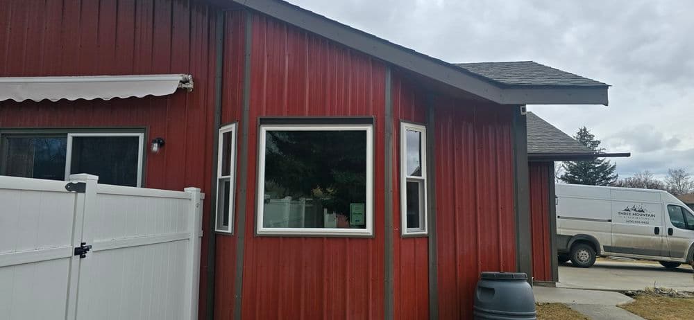 Red metal house exterior featuring multiple windows and a white fence, with a van in the background.