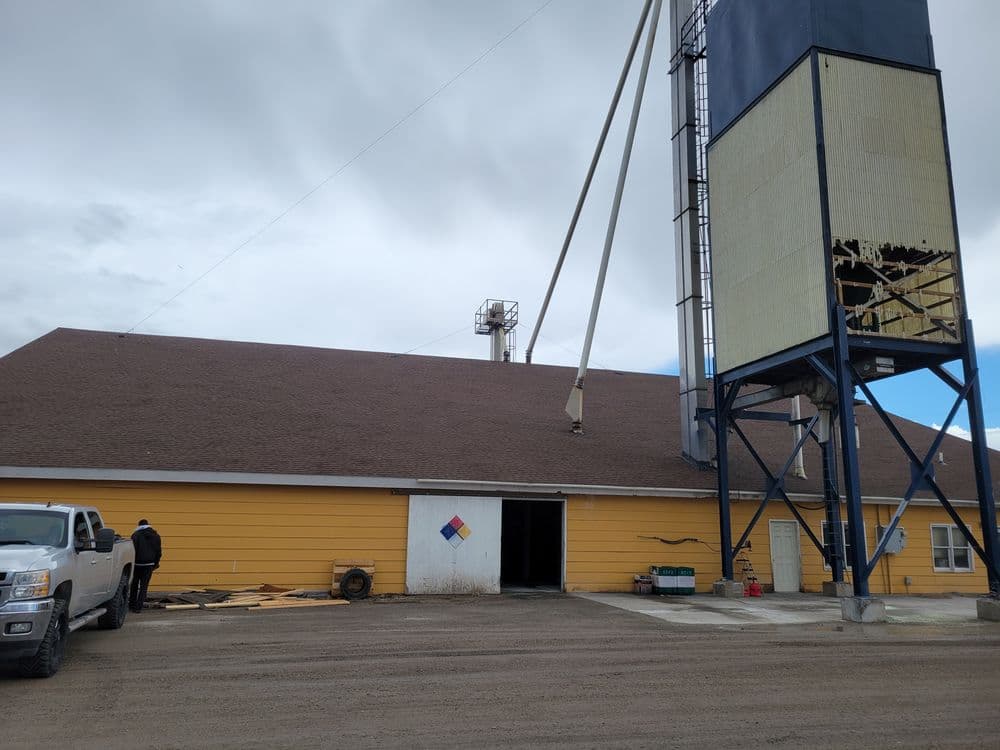 Yellow building with silo, workers outside, and construction materials visible nearby.