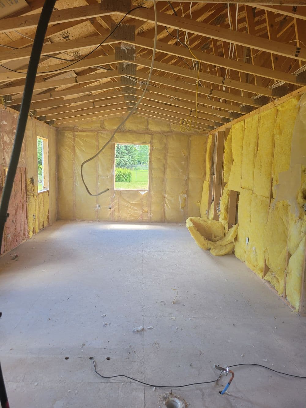Interior view of an unfinished room with yellow insulation and exposed wooden beams.