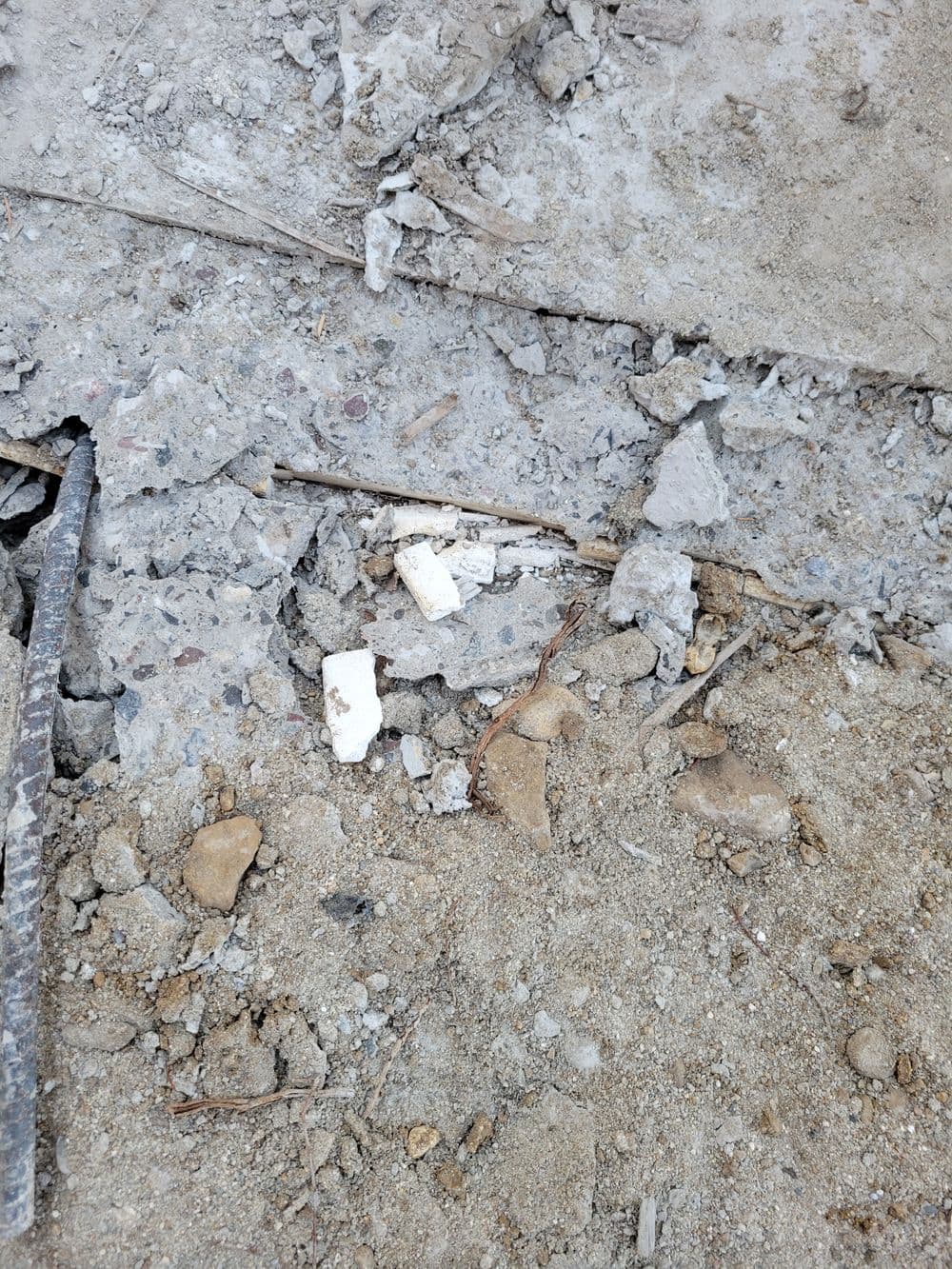 Construction debris with broken concrete and gravel on a dirt surface.