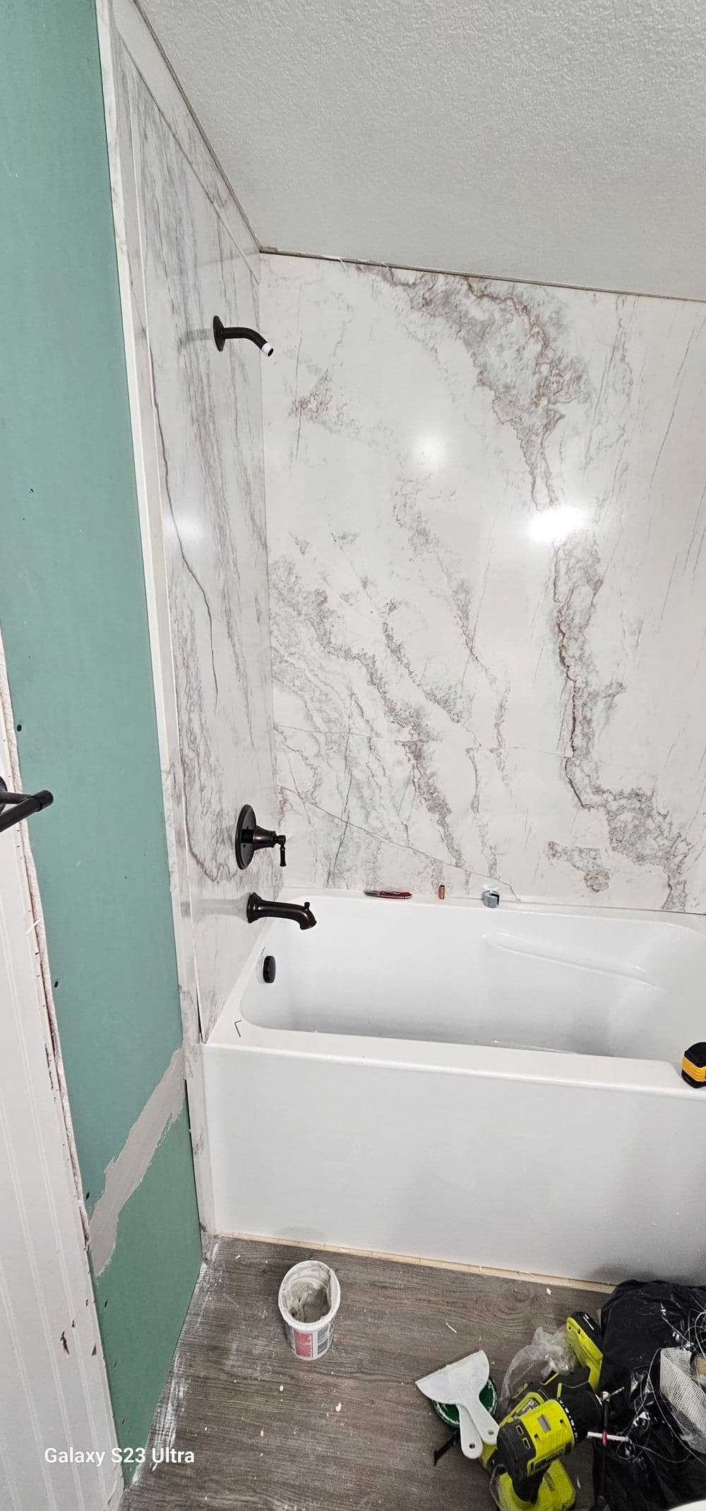 Modern bathroom renovation featuring a white bathtub, marble wall, and tools for installation.