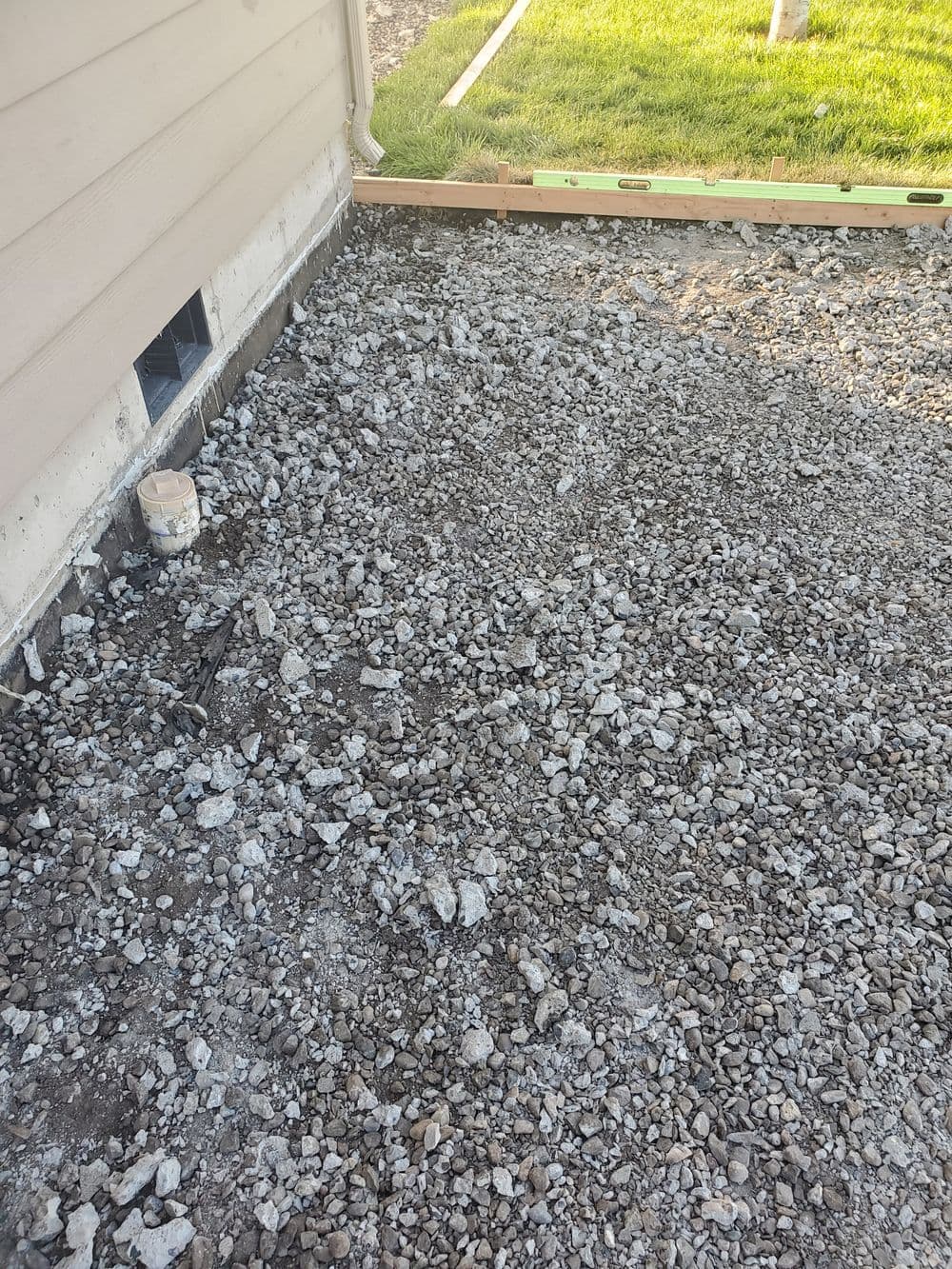 Gravel base preparation beside a house foundation for landscaping or construction.