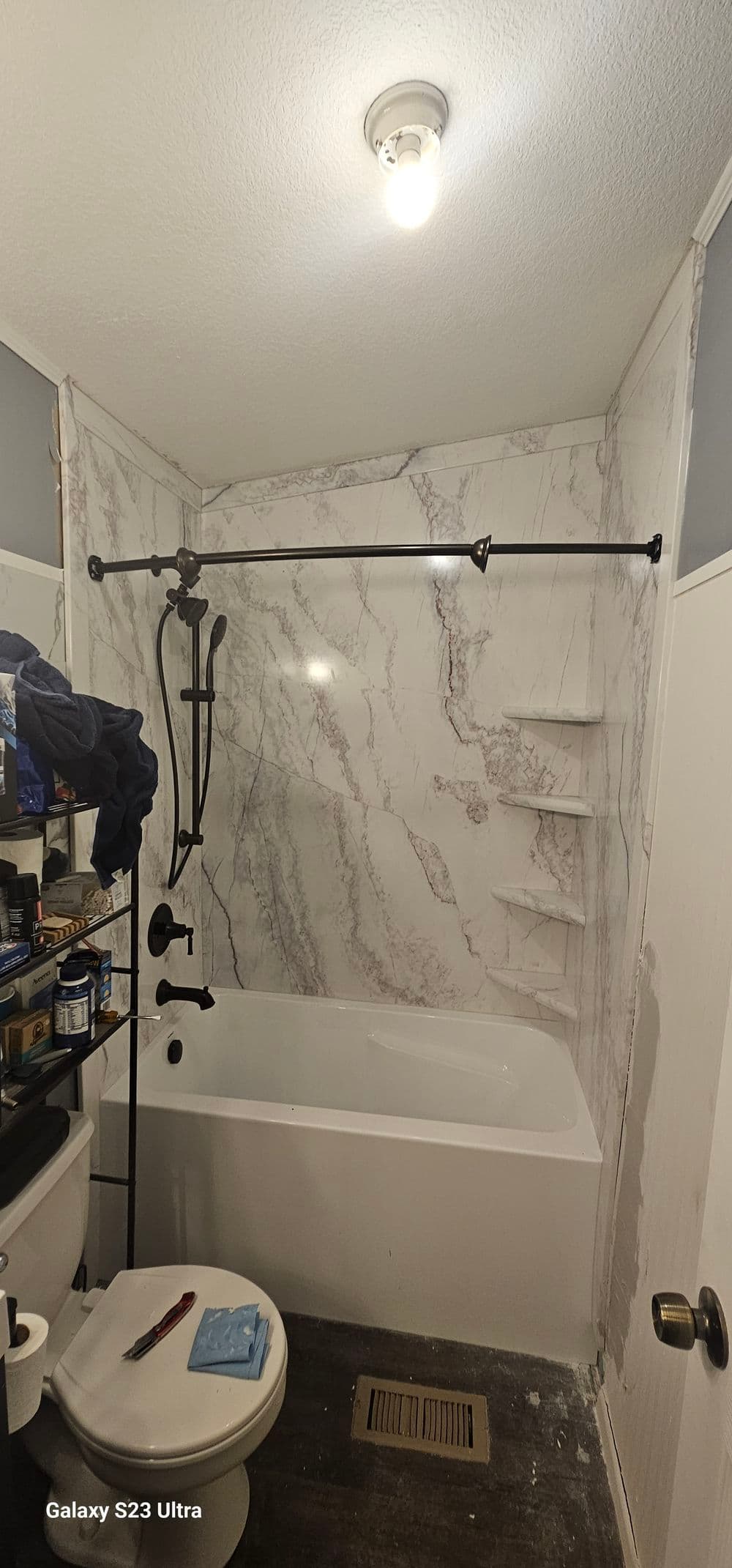 Modern bathroom with a marble accent wall, tub, shower, and organized shelf.