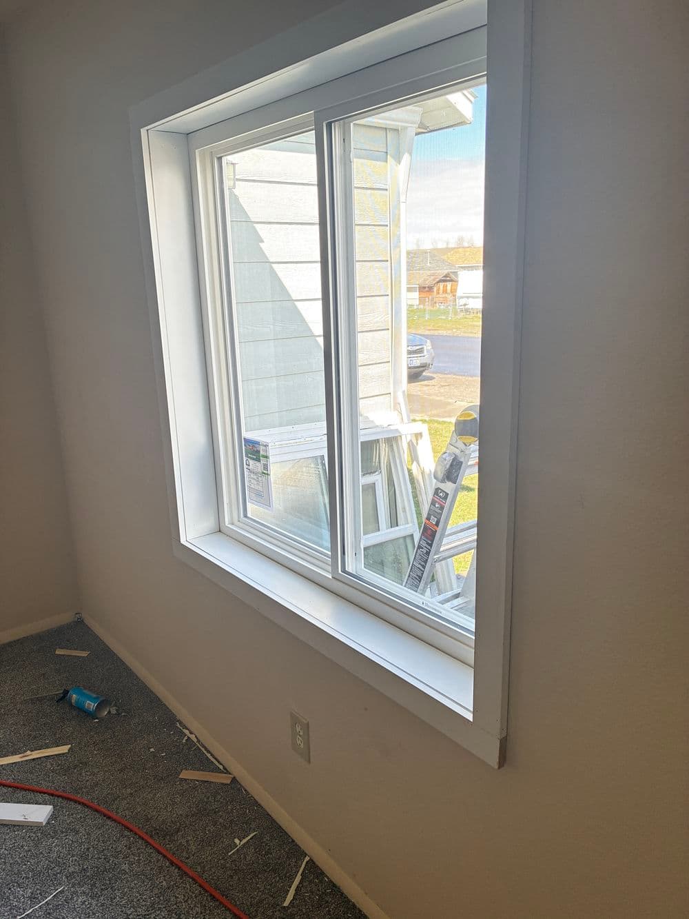 Newly installed double-pane window in a bright room with construction tools outside.