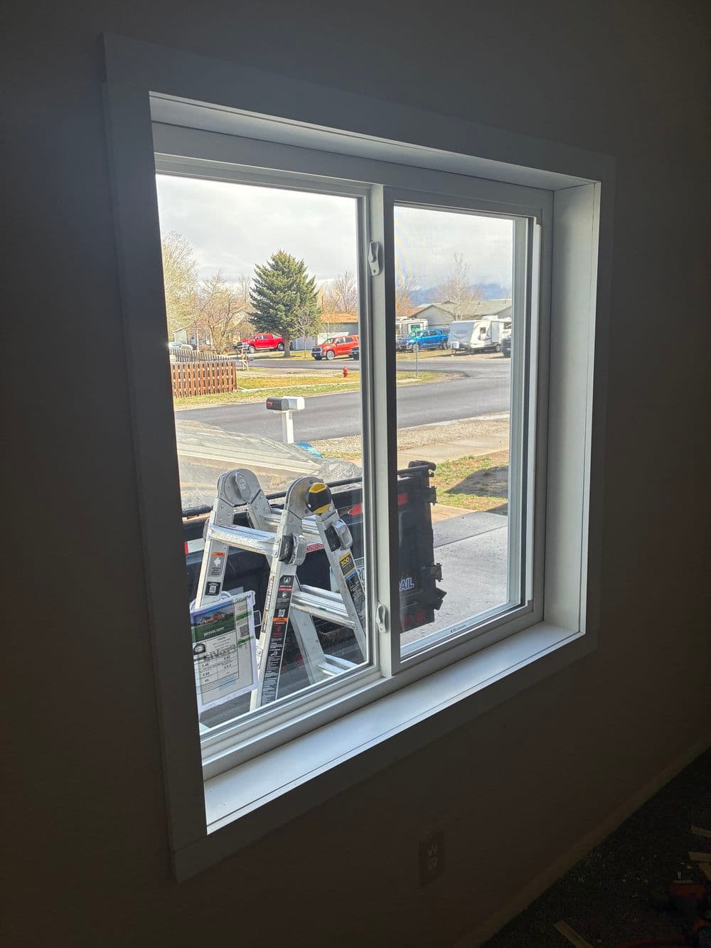 Double-hung window with outdoor view, showcasing a ladder and parked vehicles.