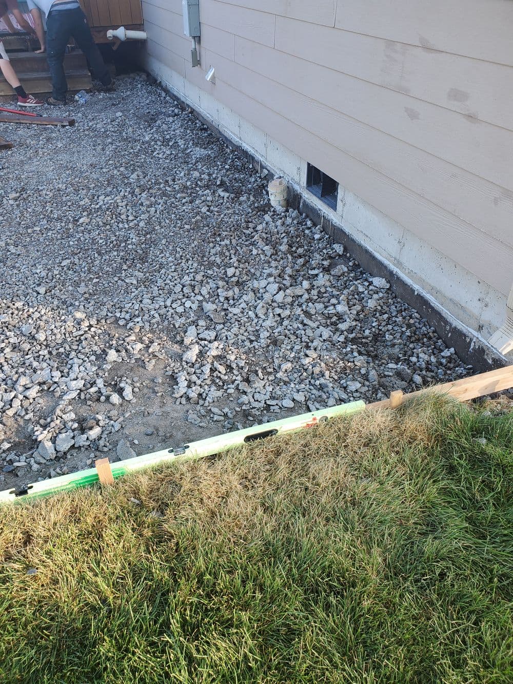 Construction site with gravel foundation preparation next to a house's exterior wall.