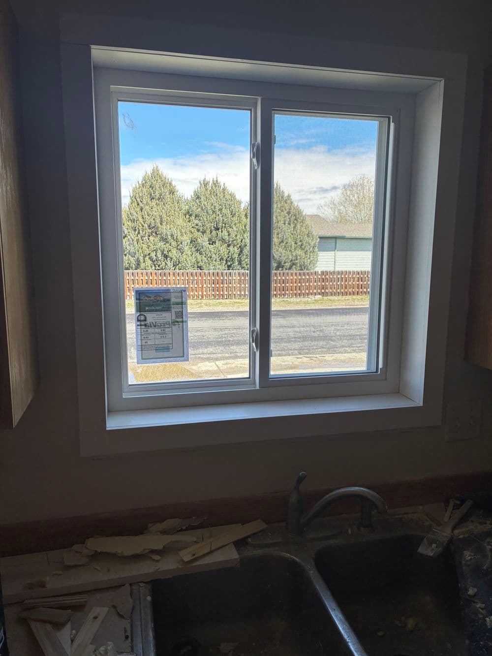 New kitchen window with view of trees and street, under renovation with debris in sink.