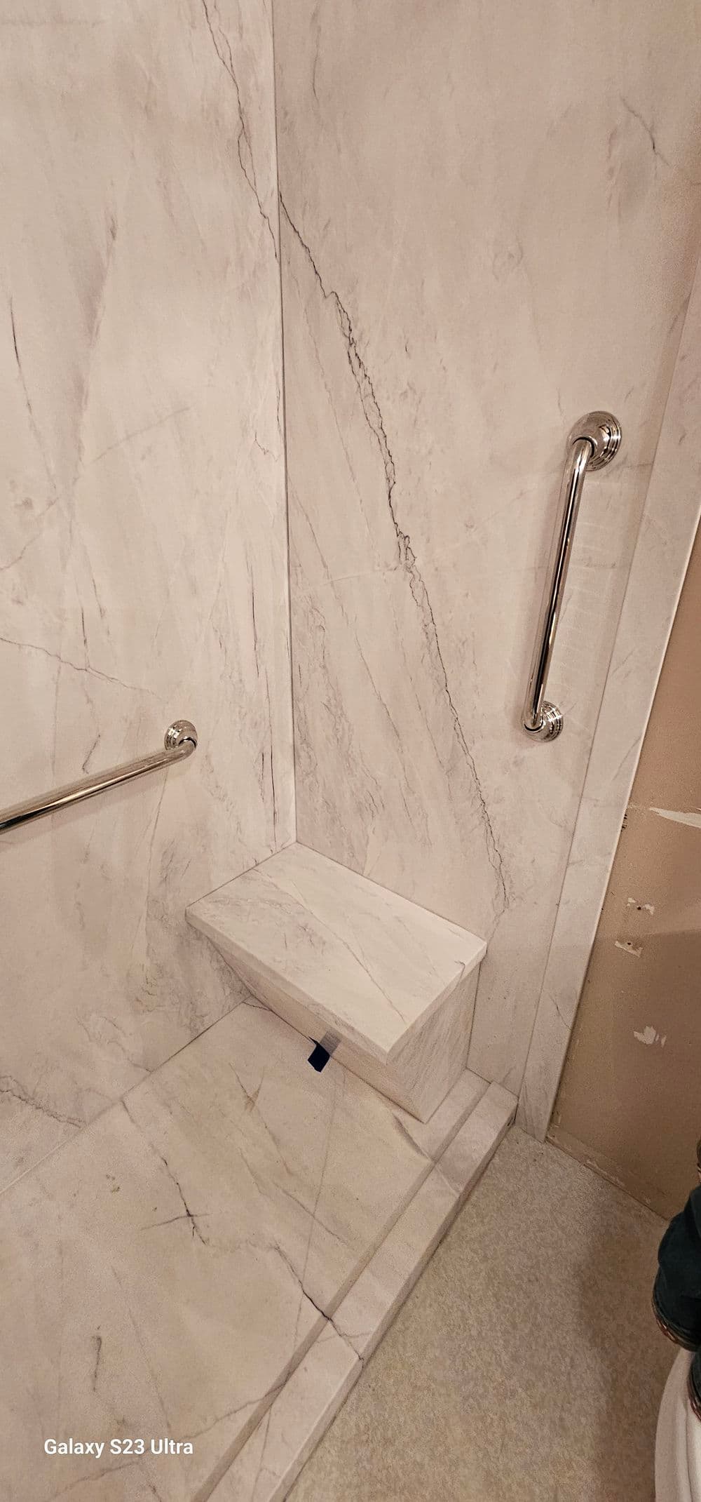 Modern marble shower design with grab bars and a built-in bench for accessibility.