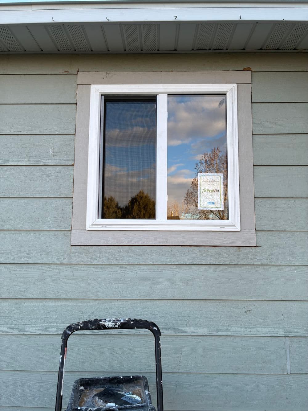 Newly painted window on light blue house exterior with painter's ladder in foreground.