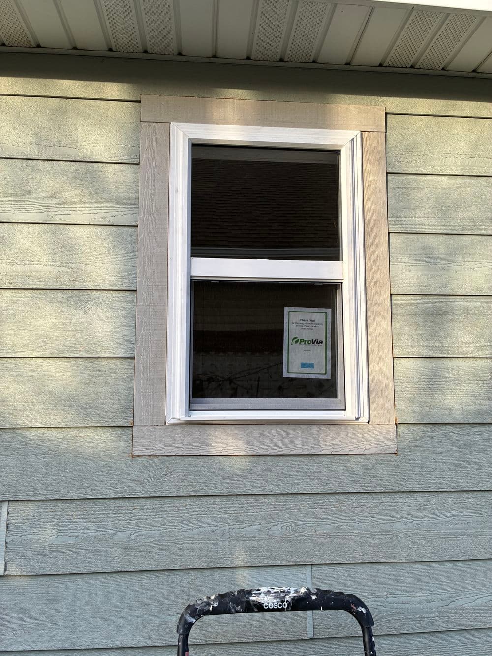 Window installation on a green house exterior with a visible safety certificate.